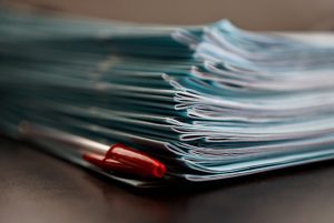 Red pen with stack of blue books for grading