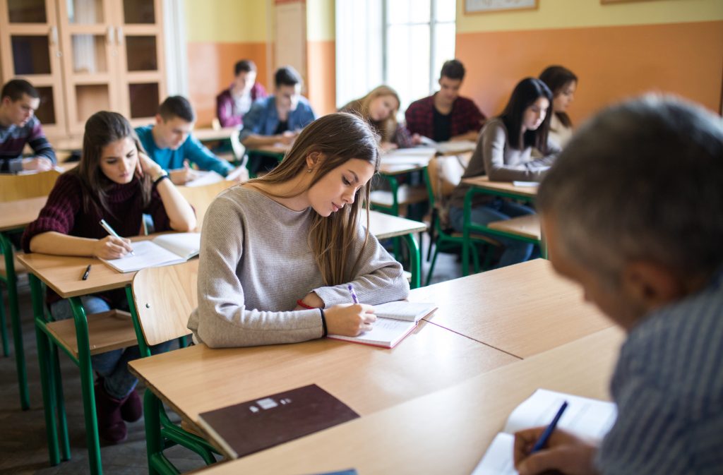 Large group of students sitting in the classroom and writing a test.