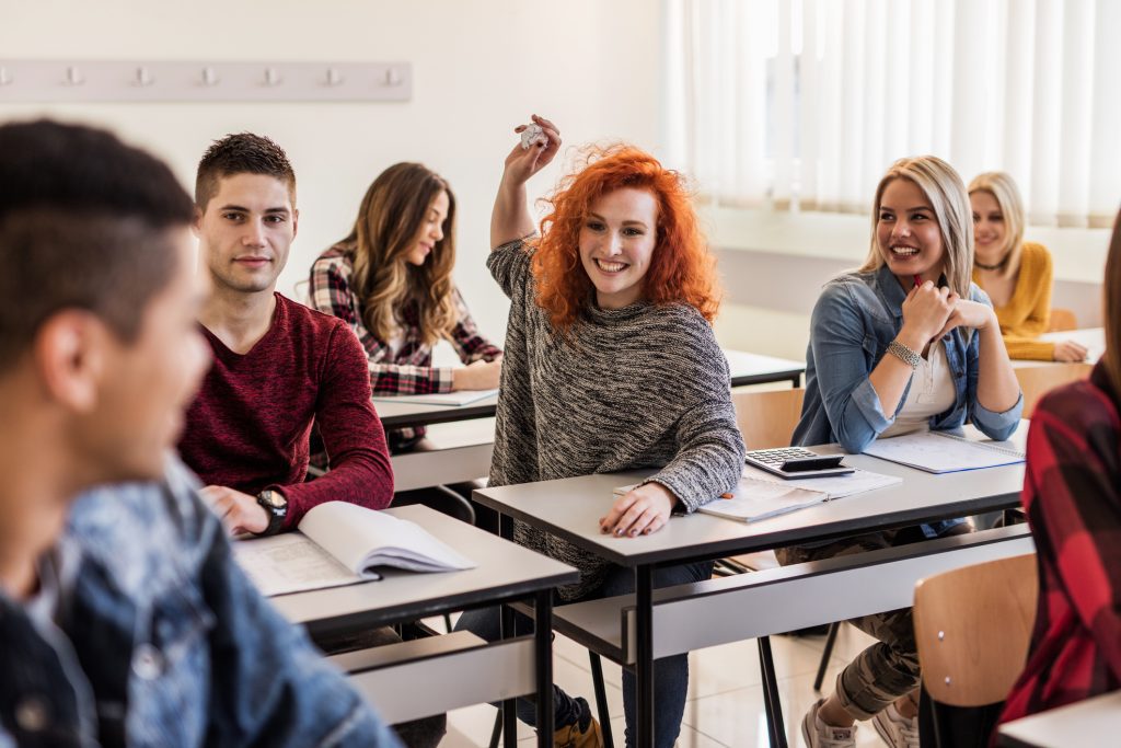 Playful female student having fun in the classroom and throwing paper on her classmates.