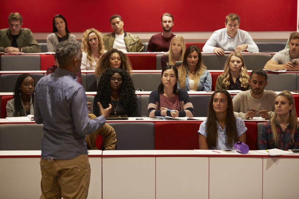 Back view of man presenting to students at a lecture theatre.