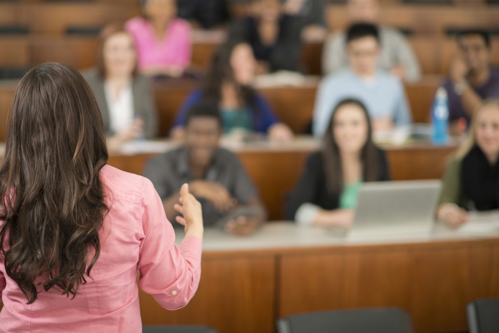 College age students are sitting in a row in a lecture hall and are listening to their professor.