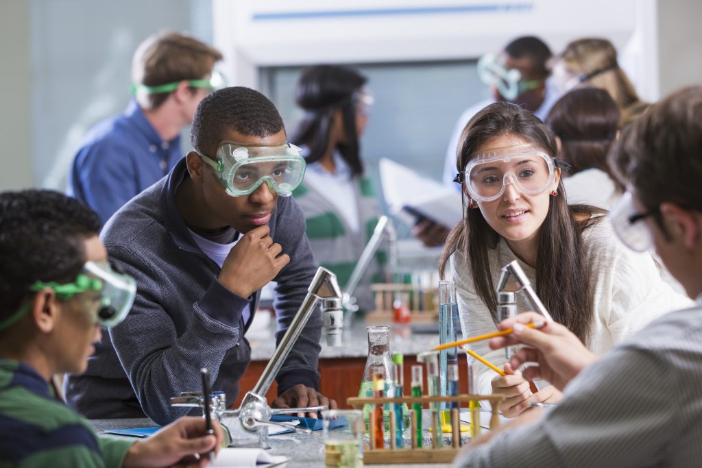 Students doing a chemistry experiment in class. The students are all wearing protective safety goggles.