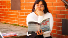 An image of a woman reading a book on the stairs with a brick wall behind her. 