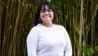 An image of woman with black hair and glasses smiling with bamboo behind her. 