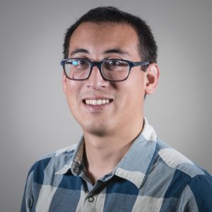 A photo of Chris. He has dark glasses, short hair and is wearing a blue flannel patterned shirt.