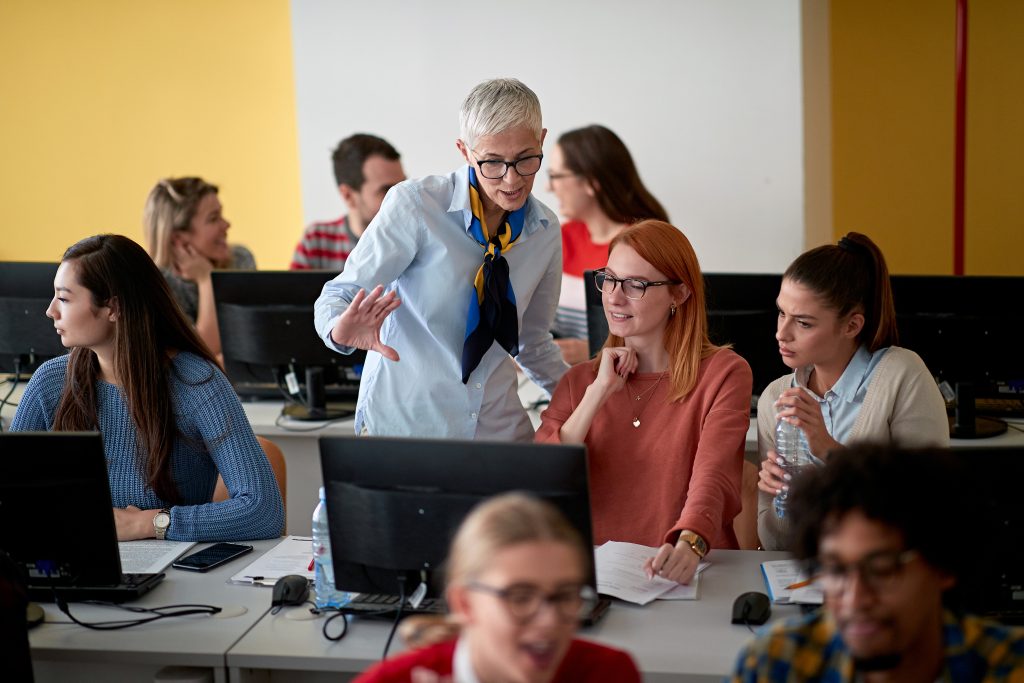 Female professor inspecting the work of students at an informatics lecture in the university computer class room